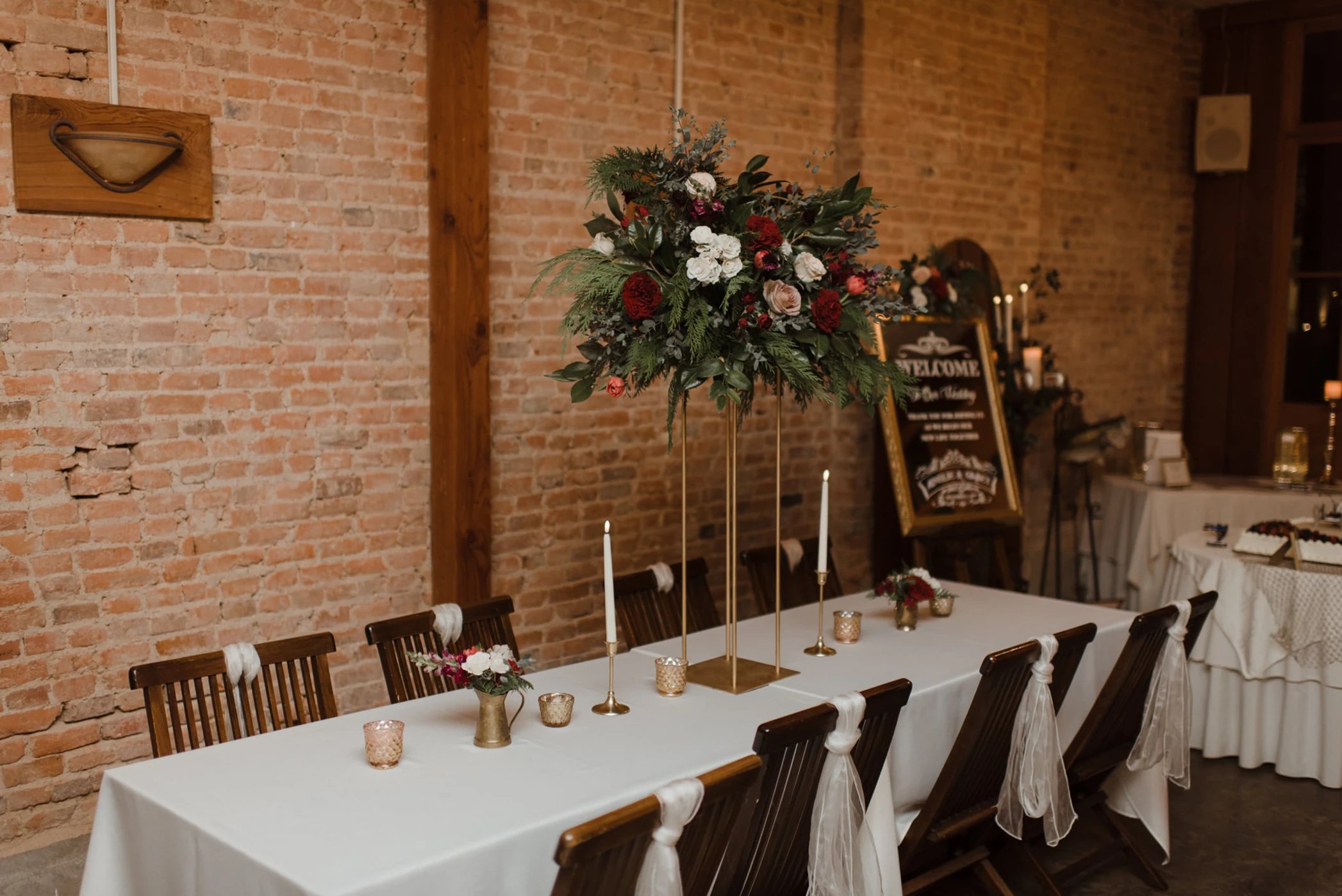 Wedding reception table with tall floral centerpiece against exposed brick wall at Maison De Tours Saint Martinville Louisiana